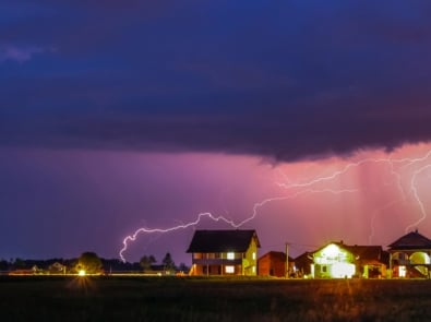 Thunderstorms with a purplish hue striking lightning over a well lit neighborhood.