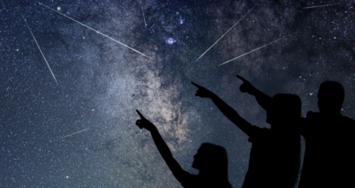 Silhouette of three people pointing at meteors in sky at night.