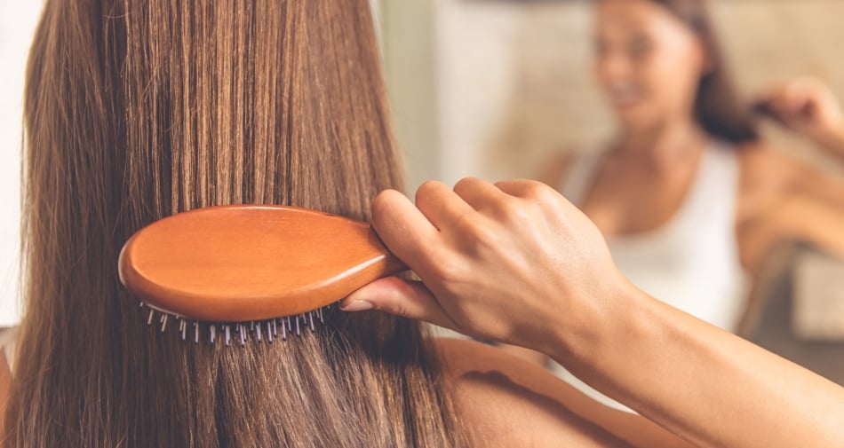 Woman brushing hair in front of mirror with a wooden brush.