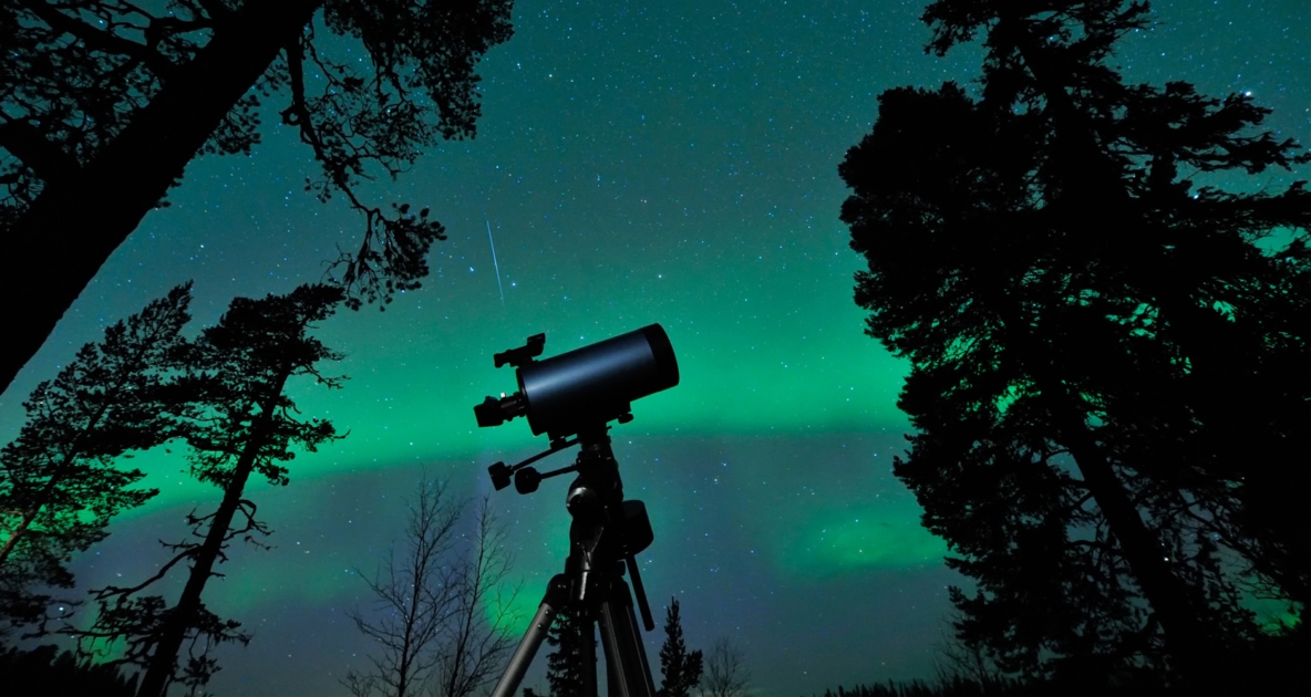 Northern lights appearing over a telescope in a forest.Telescope