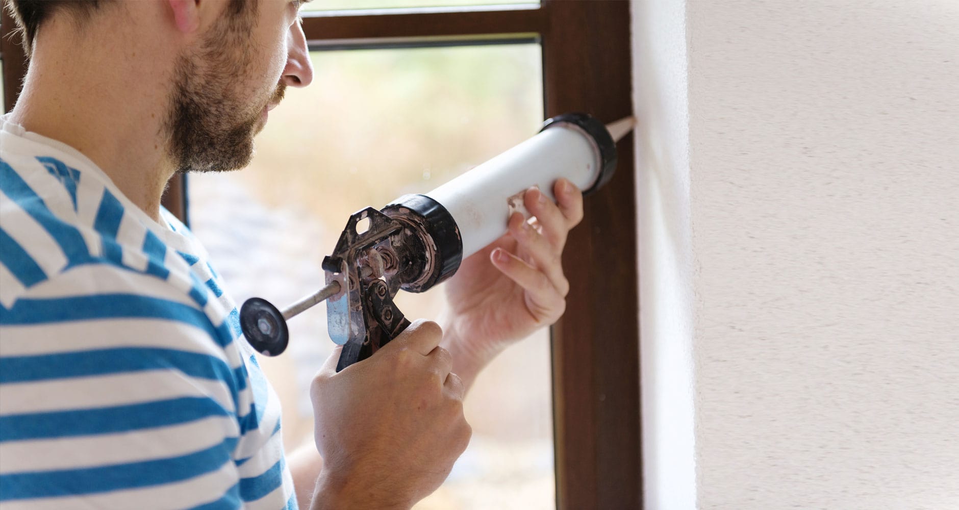 Caulking a window frame to seal entry points and keep spiders out of your house
