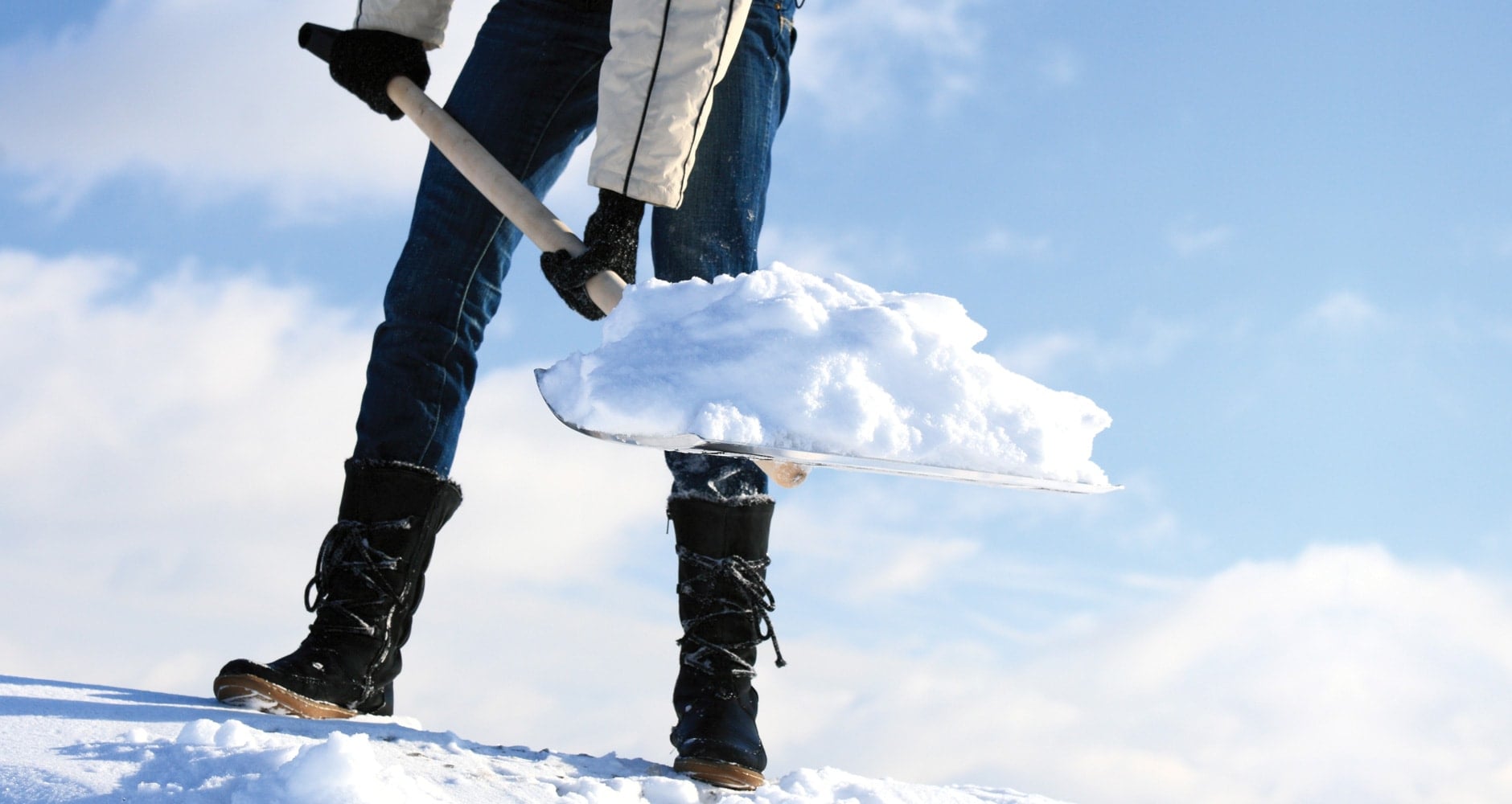 A person shovels a snowy driveway, illustrating the safety tips to avoid heart strain.