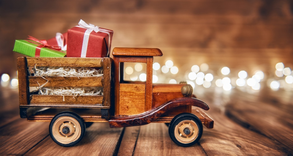 A vintage wooden toy ruck carrying a load of presents with candles in the background.