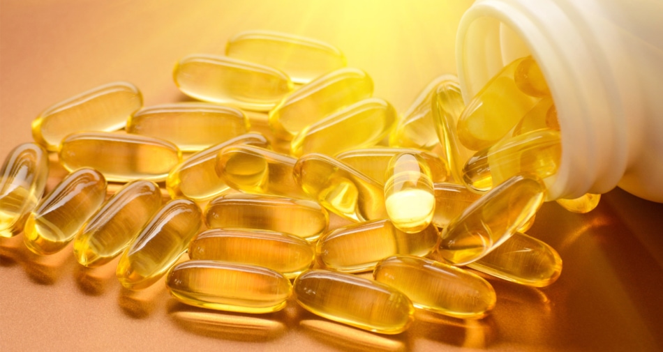 Gold colored vitamin capsules spilling out of a bottle.