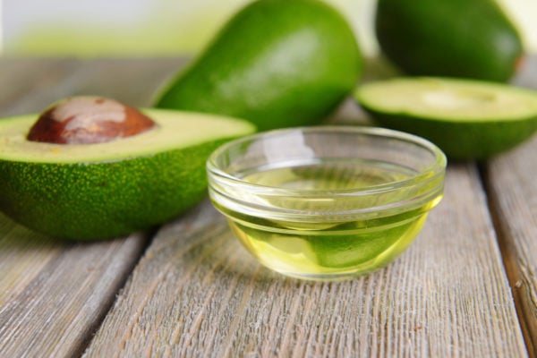 avocado oil in a small bowl with sliced avocados in the background