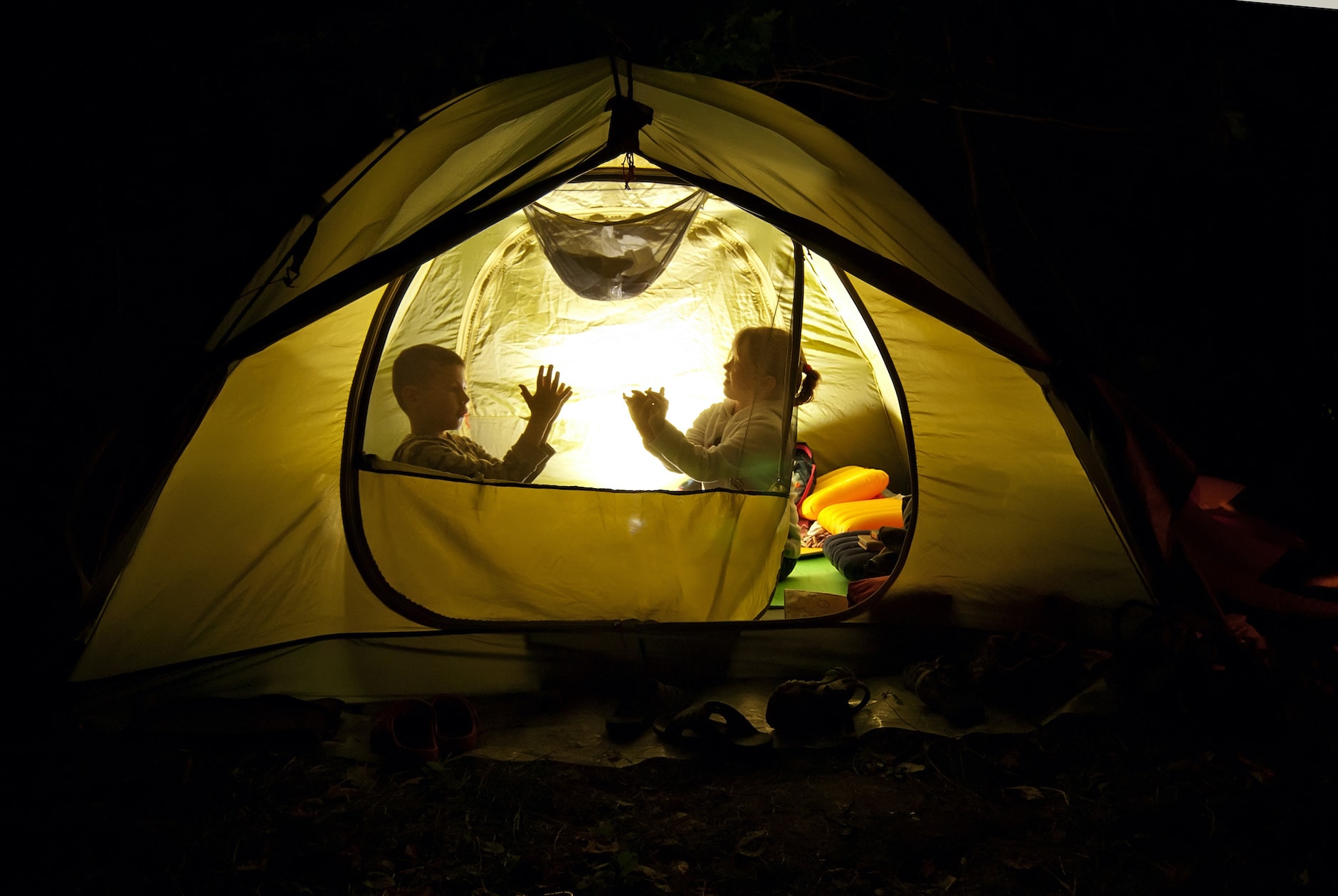 two kids camping out in a yellow tent at night