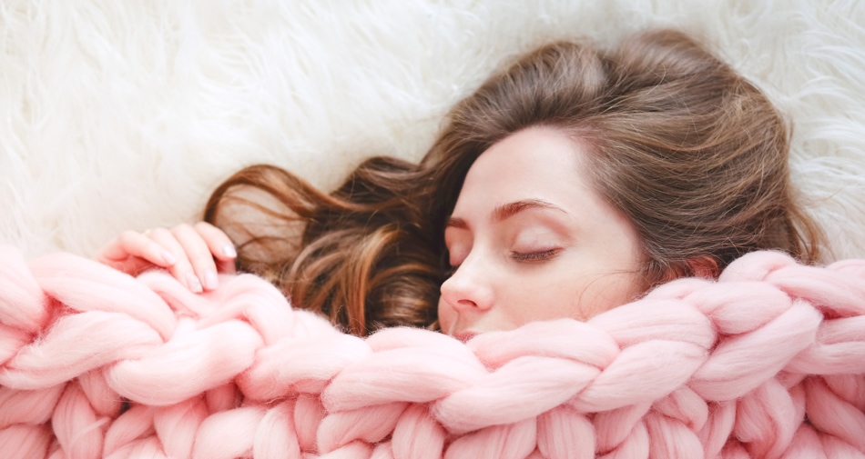 Woman with brunette hair sleeping behind pink covers.