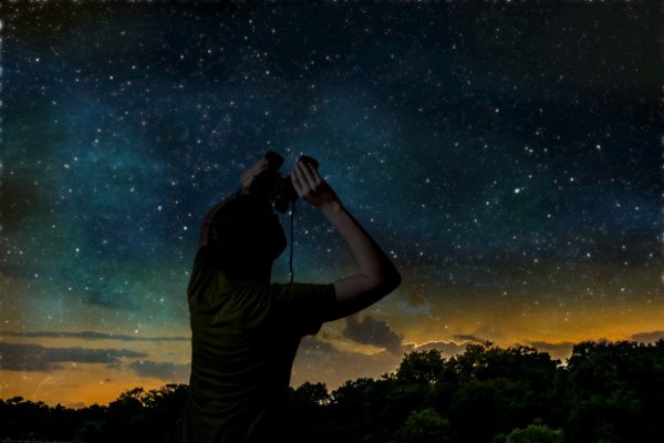 person looking up in the night sky with binoculars