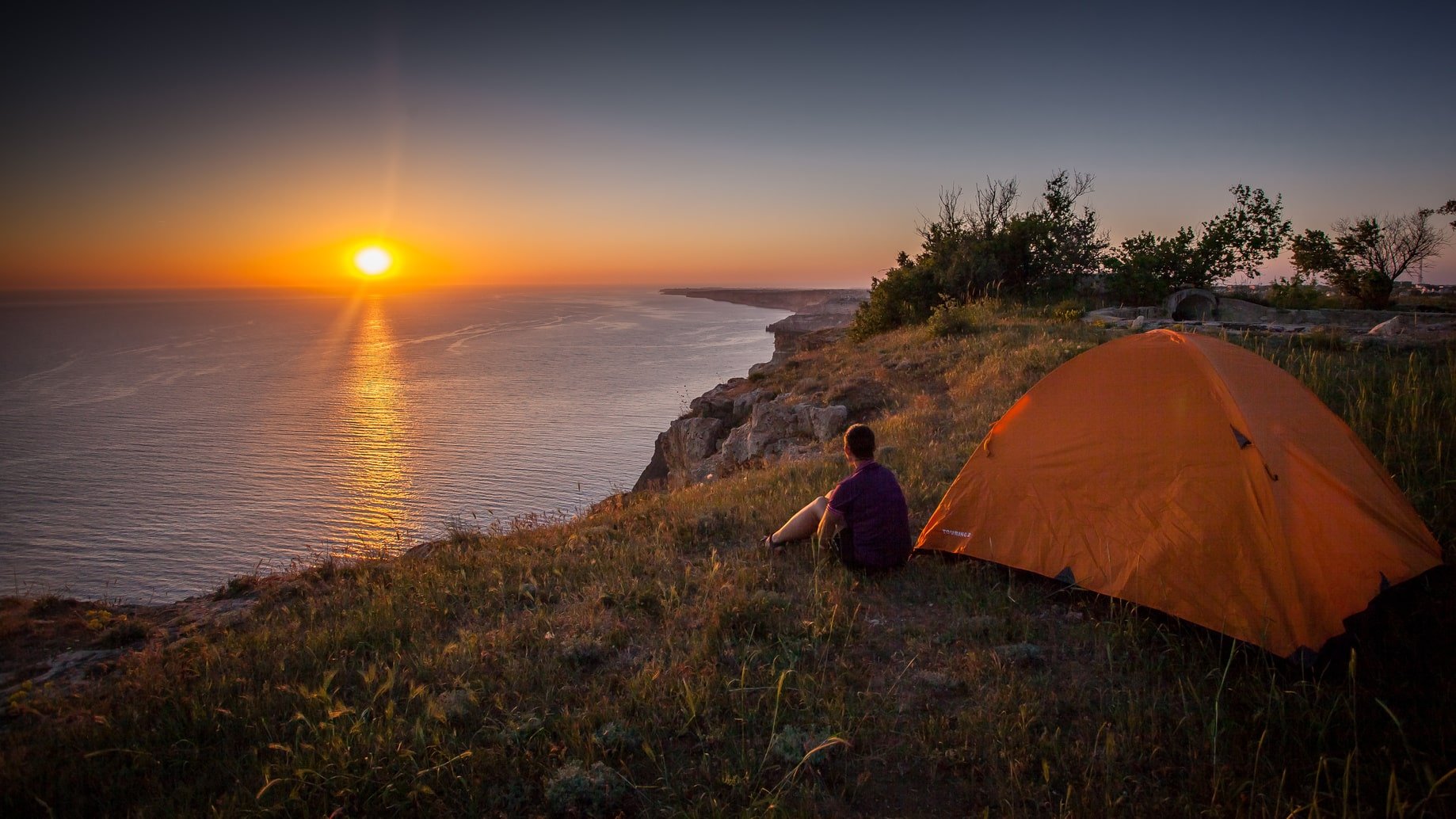 Great American Campout - person sitting next to tent watching a sunset over the ocean