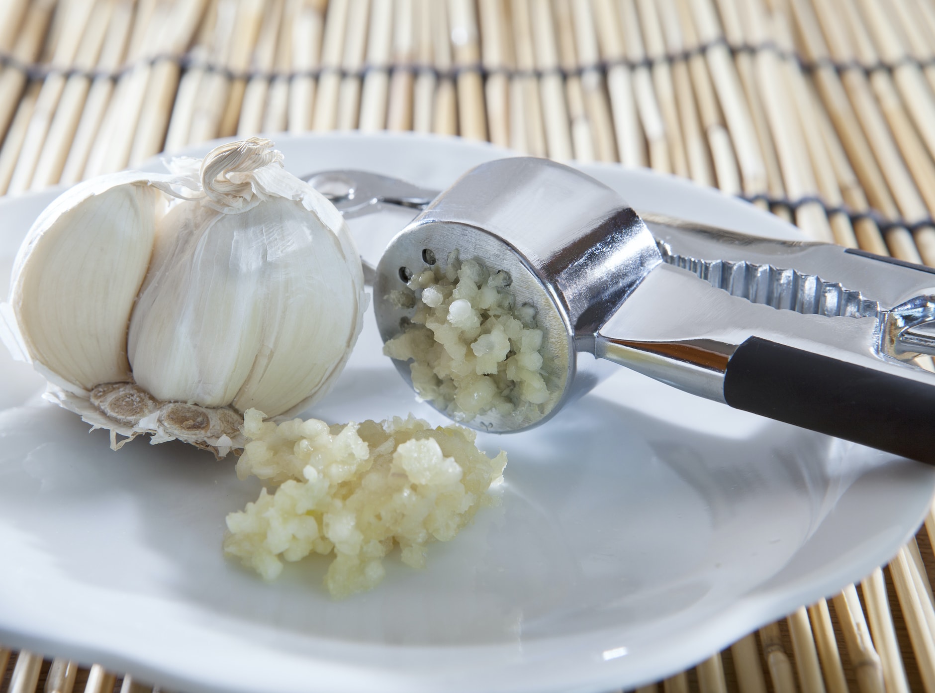 fresh garlic crushed by garlic crusher on white dish on kitchen table top use for food spice and ingredient healthy topic