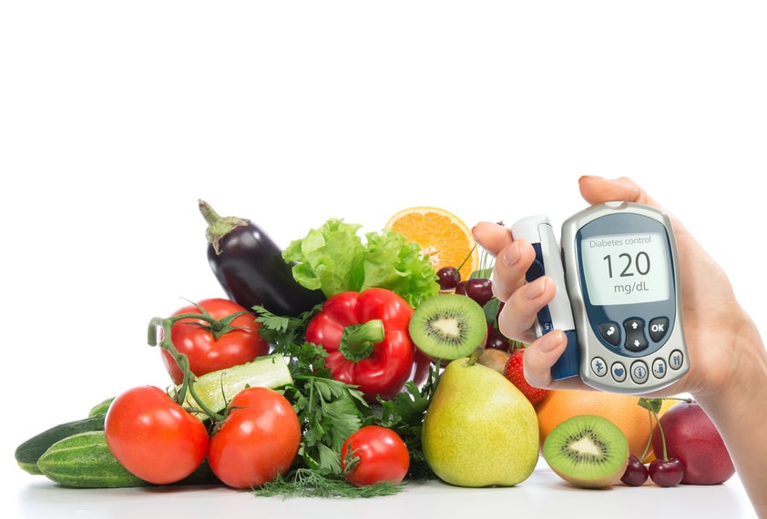 Glucose meter in hand in front of fruits and vegetables.