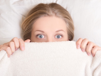 Funny young woman lying in bed under blanket.