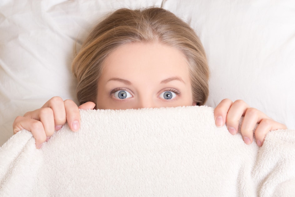 Funny young woman lying in bed under blanket.