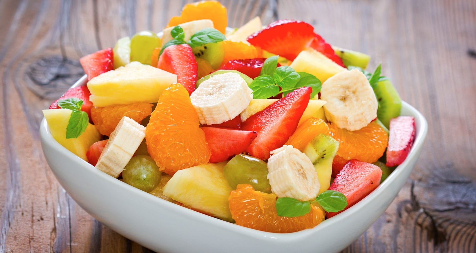 Fresh fruit salad with mint in a bowl on a wooden table.