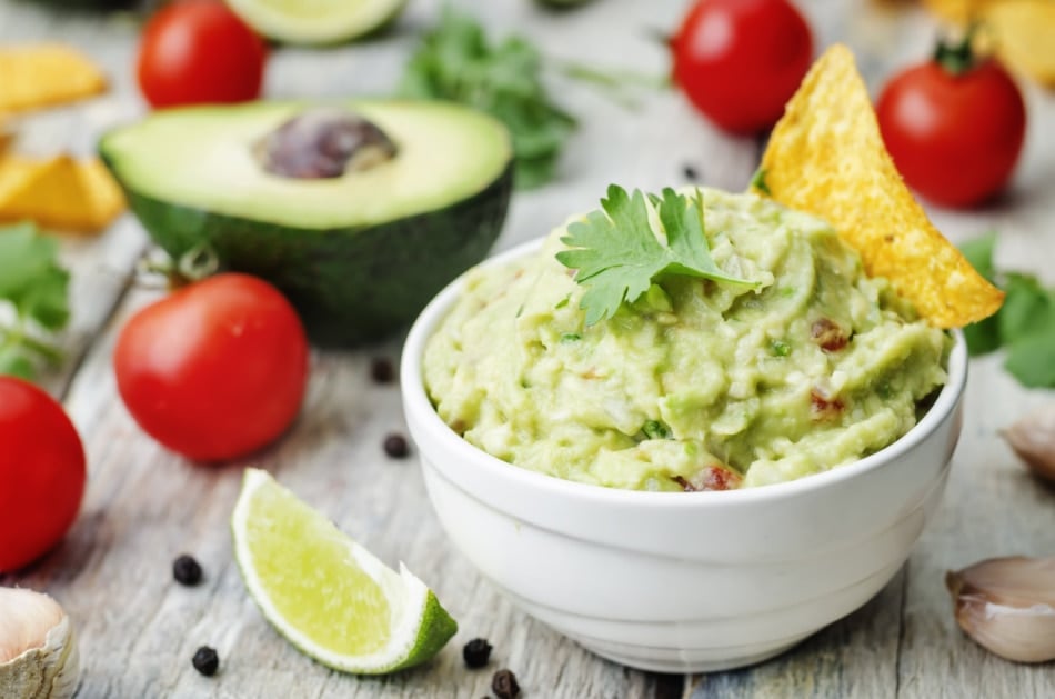 Guacamole with corn chips on a white wood background.