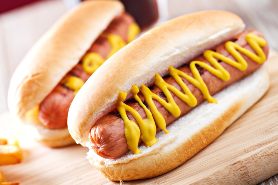 Hot Dogs in buns topped with mustard.