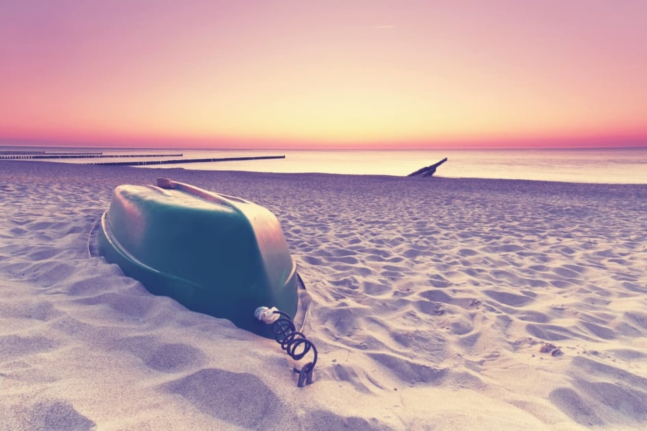 Rowboat stored upside down on a sandy white beach.