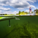 Fishing lure shown up close and under water with fisherman on boat in background.
