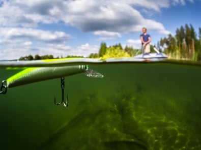 Fishing lure shown up close and under water with fisherman on boat in background.