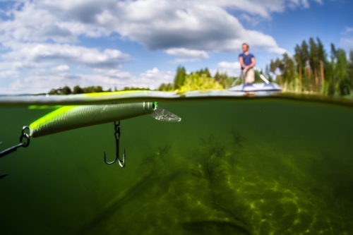 Fishing lure shown up close and under water with fisherman on boat in background.