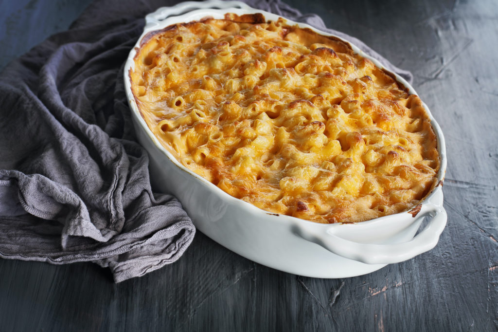 High angel view of a dish of fresh baked macaroni and cheese with table cloth and old wood spoon over a rustic dark background.