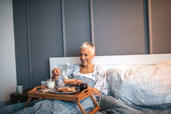 Mom with short gray hair enjoying mother's day breakfast in bed with toast and coffee
