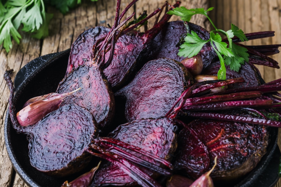 Homegrown roasted beets and garlic in cast iron skillet, fresh parsley herbs on wooden rustic table, plant based food, local produce, close up. Organic vegetables,  healthy  vegan eating, harvest time.