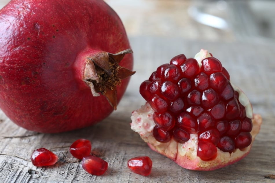 Fresh pomegranate seeds and pomegranate slices on wooden background.