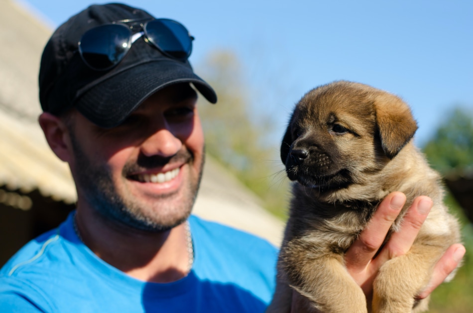 Man with a baseball cap holding a puppy.