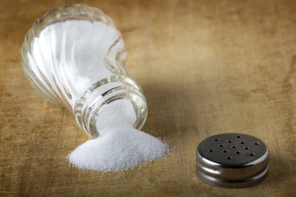 Salt shaker with spilled salt on the wooden table