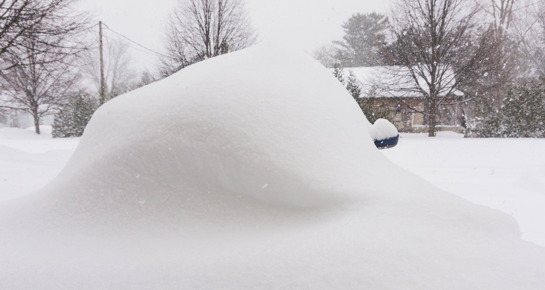 snow mound in a neighborhood with house behind it and snowflakes falling