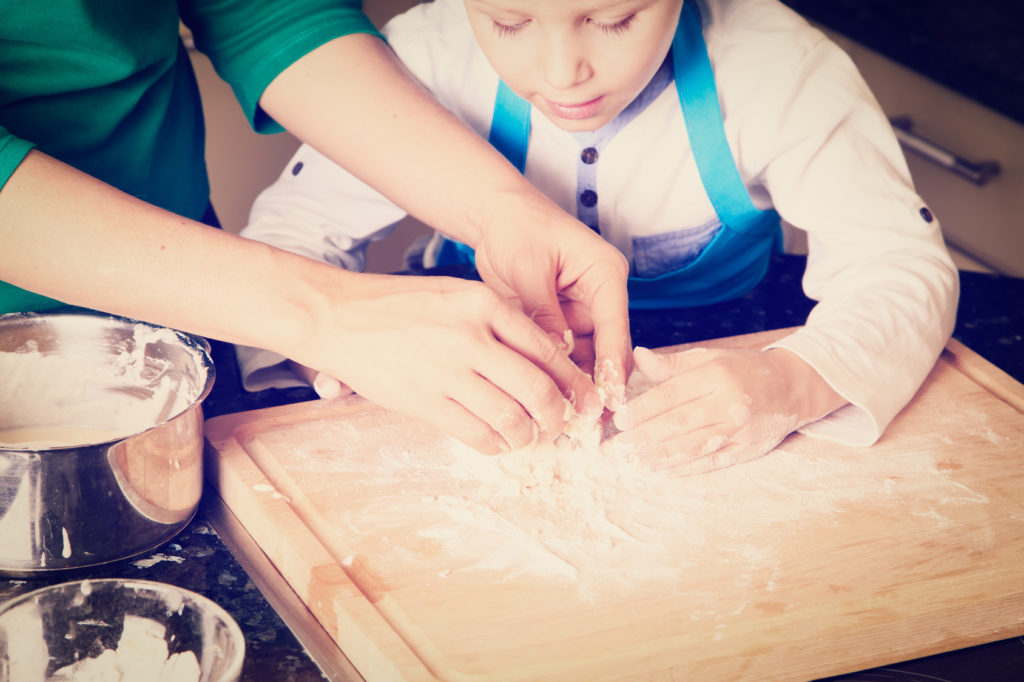 hands of mother and son kneading dough on wooden table