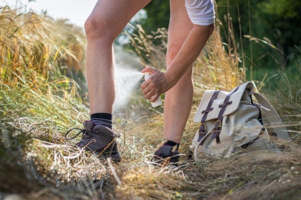 person spraying insect repellent on her legs