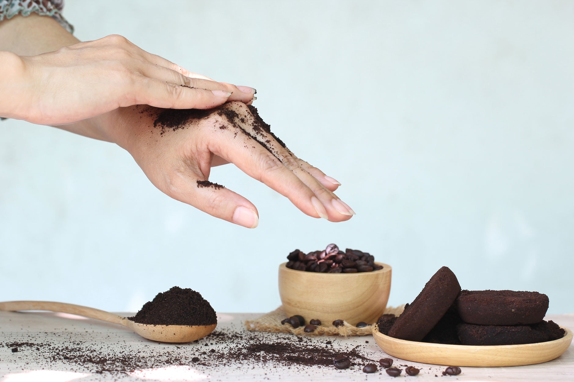 A jar of homemade coffee ground body scrub on a bathroom shelf with a wooden spoon.