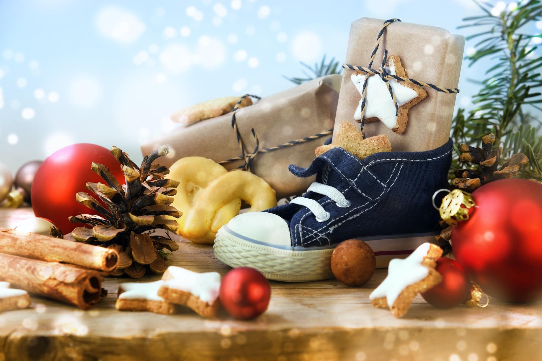 St. Nicholas Day, Children's shoe with sweets, gifts and christmas ornaments on rustic wood, light blue snowy background, in Germany called Nikolaus, selected soft focus