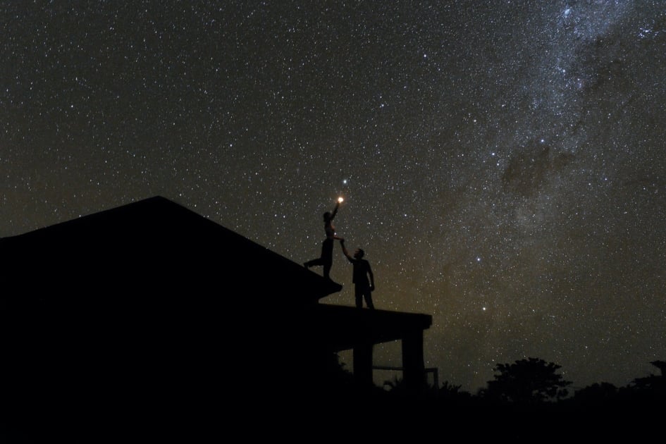 Couple shining flashlight at Milky Way from a rooftop.