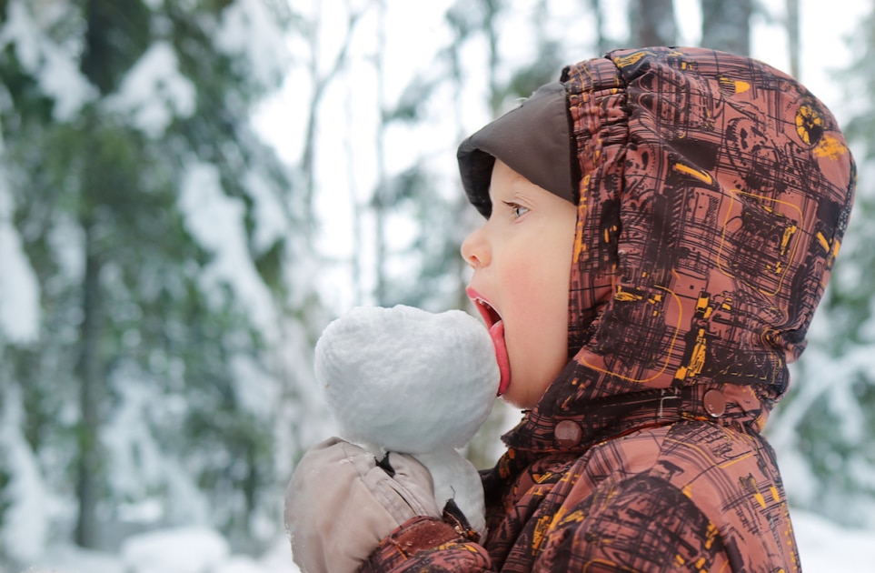 Little happy baby eating snow.