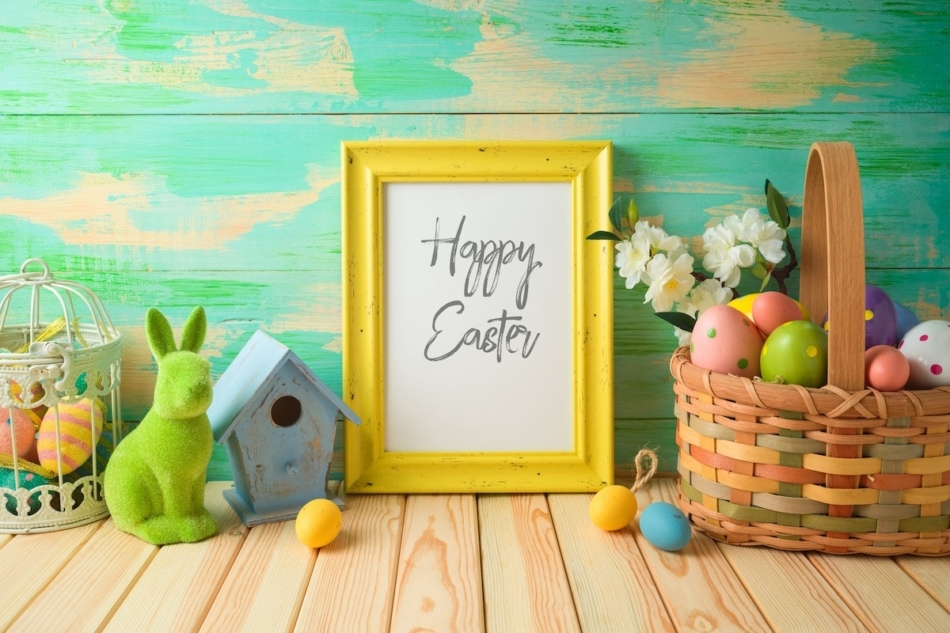 Photo frame saying Happy Easter on wooden table with Easter decorations.