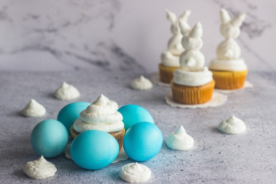 Blue Easter eggs surround cupcakes along with bunny shaped white cupcakes.