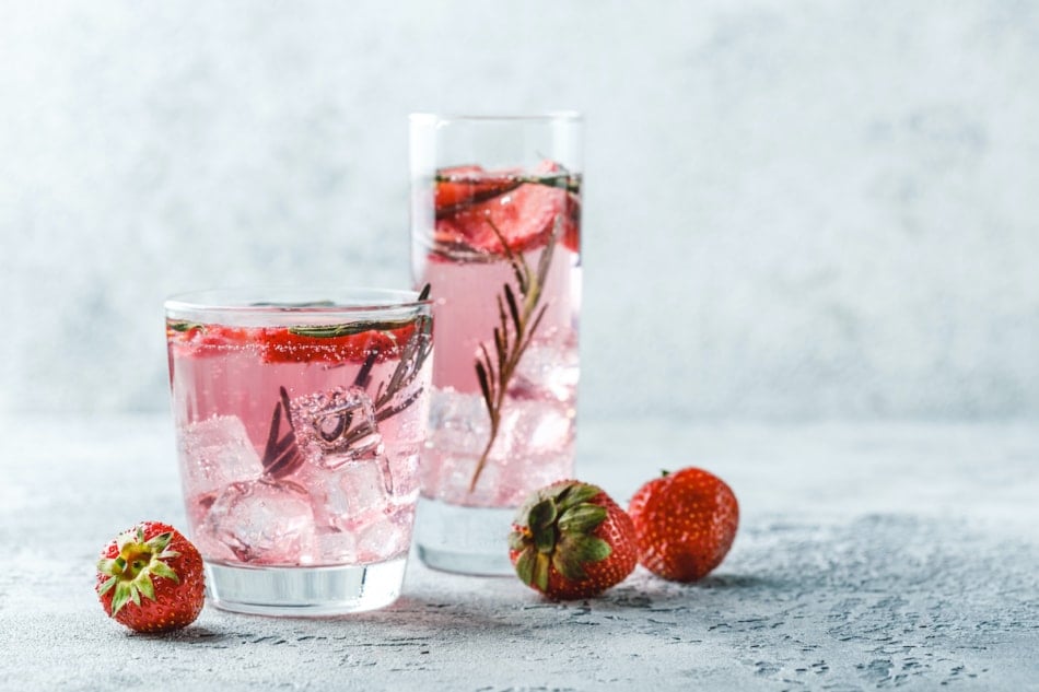 cocktail with strawberry tops and rosemary and ice in glass glasses.