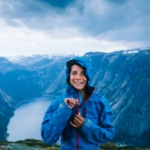 Happy woman zip up blue sportive jacket before rain, get ready for adventure and smiling in cliff during trip Norway. Trolltunga hiking route