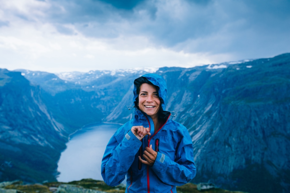 Happy woman zip up blue sportive jacket before rain, get ready for adventure and smiling in cliff during trip Norway. Trolltunga hiking route