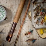 Salmon flies, split cane fly fishing rod and reel on a rustic white wooden background