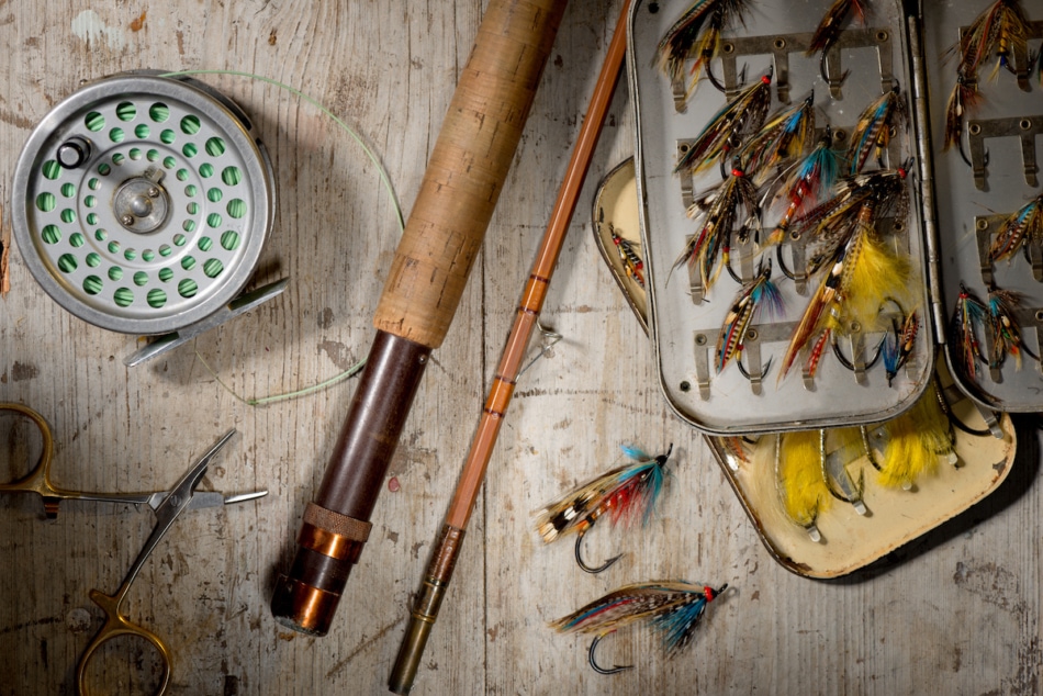 Salmon flies, split sugarcane flying fishing rods and scrolls on the rustic white wooden background