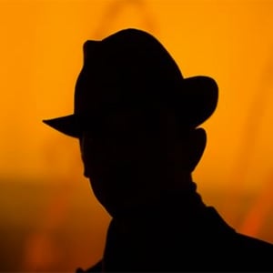 Silhouette of mystery man wearing a hat against an orange background.