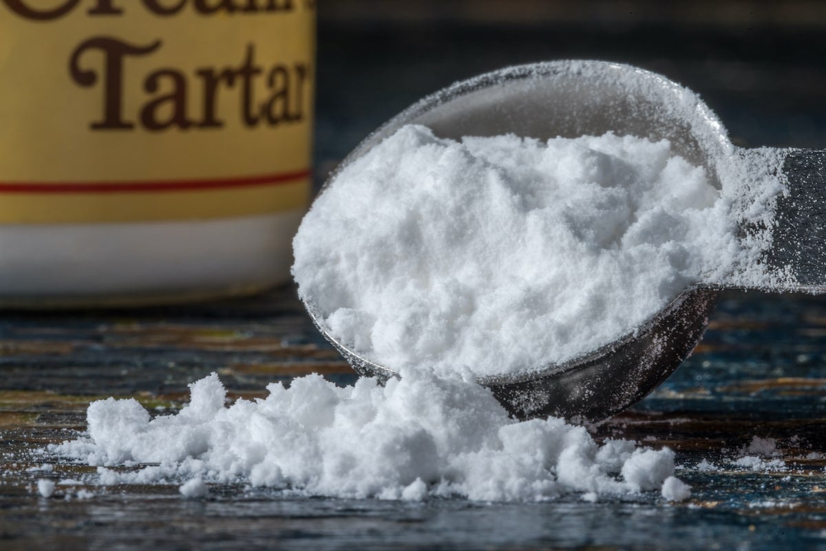 Cream of tartar in a small dish on a wooden countertop, a pantry-staple natural bug repellent that turns back marching ants at the threshold