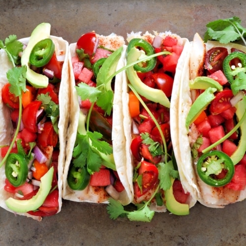 Spicy fish tacos with watermelon salsa and avocados, above view on rustic metallic background