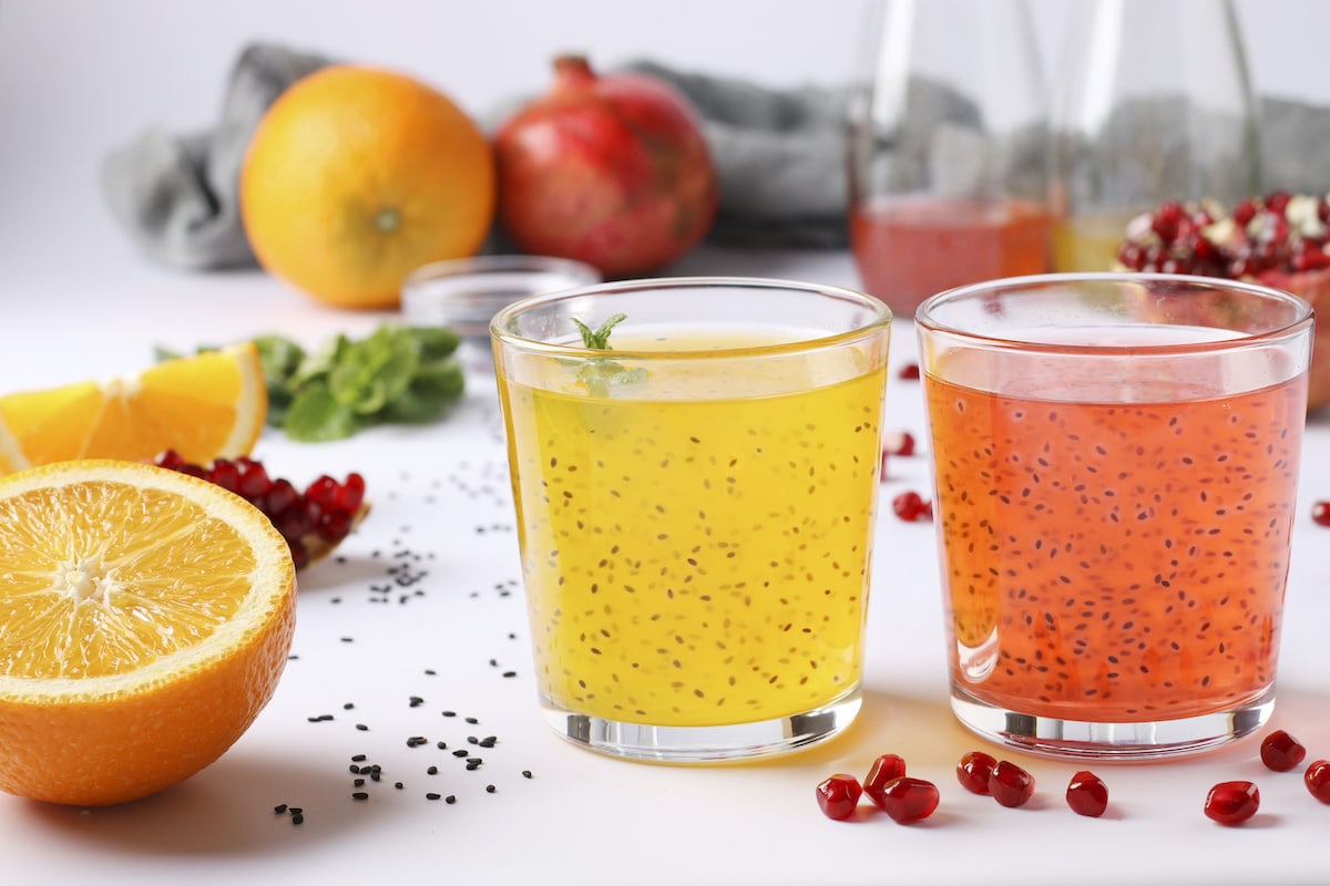 Tropical orange and pomegranate juice with basil seeds or falooda seeds or tukmaria in glasses and bottles on white background, Closeup