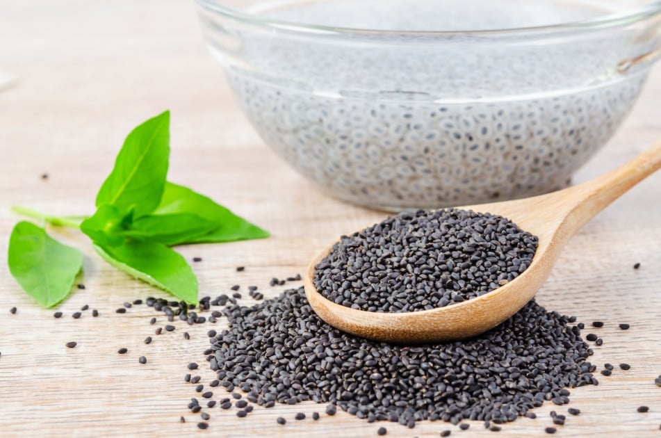 basil seeds in wooden spoon and soak in water with green leaf on wooden background.