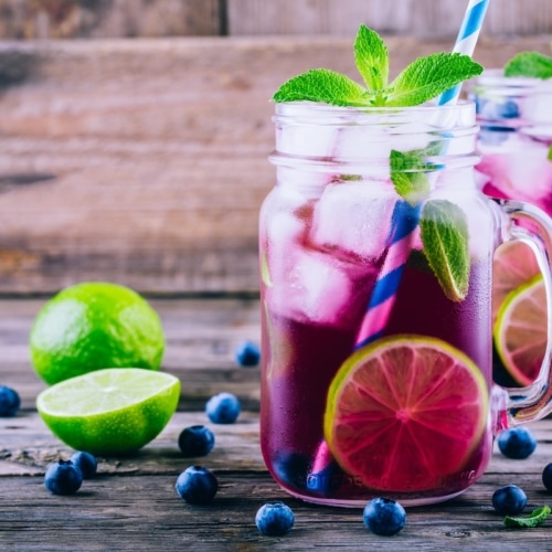 Blueberry ice mojito with lime and mint in mason jar on wooden background